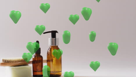 Animation-of-green-hearts-rising-over-soap,-brush,-self-care-and-beauty-products-on-beige-background