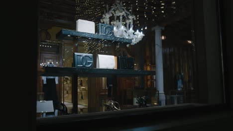 nighttime-view-inside-a-luxury-boutique,-showcasing-designer-handbags-on-illuminated-shelves-under-a-chandelier
