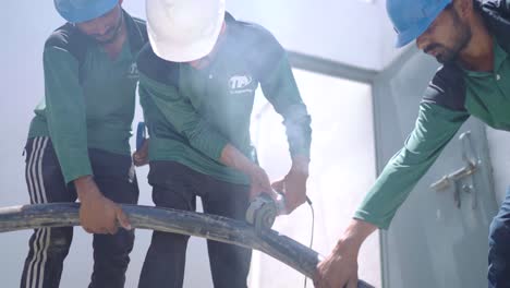 Group-Of-Engineers-Using-Angle-Grinder-To-Cut-Thick-Cable-Held-Up-By-Colleagues-At-Warehouse-In-Pakistan