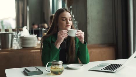 Una-Mujer-Hermosa-Bebe-Té-Y-Reflexiona-Mientras-Está-Sentada-Con-Su-Computadora-Portátil-En-Un-Restaurante