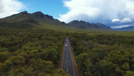 4k-drone-video-flying-forward-through-lush-green-nature-following-a-white-camper-van-driving-towards-The-Grampians-National-Park-in-Victoria,-Australia