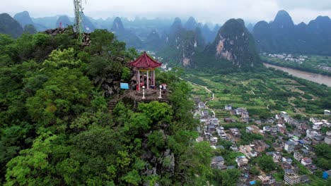 Aerial-orbit-shot-around-a-couple-of-hikers-in-a-small-pagoda-in-Laozhai-Hill-revealing-whole-Xingping-and-its-mountainous-environment