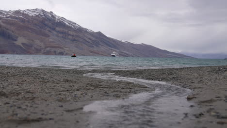 Glacial-Stream-Water-Flowing-Into-Cold-Arctic-Sea-With-Cruise-Ship-and-Coast-of-Greenland-in-Background