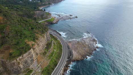 4k-Drone-Video-panning-down-to-show-the-incredible-views-of-the-sea-cliff-road,-putting-the-focus-on-the-road-as-it-curves-around-the-beautiful-Australia-landscape-next-to-the-stunning-blue-ocean