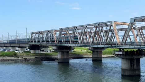 Ein-Zug-überquert-An-Einem-Klaren-Tag-Eine-Stahlbrücke-über-Einen-Ruhigen-Fluss