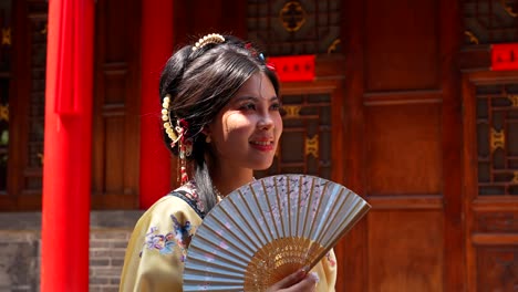 Woman-in-traditional-Qing-Dynasty-clothing-holding-a-fan,-standing-in-Pingyao-on-a-sunny-day