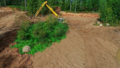 Excavator-machine-working-in-a-green-pine-forest-removing-earth,-revealing-aerial-shot