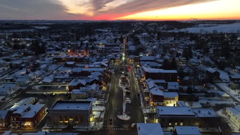 Aerial-view-of-a-snow-covered-town-at-dusk,-highlighting-the-glowing-street-lights-and-a-vivid-sunset