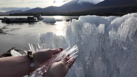 A-person-stands-by-a-body-of-water,-holding-a-piece-of-ice