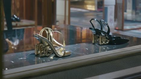 Exhibición-De-Elegantes-Zapatos-De-Tacón-Alto,-Con-Pares-Negros-Y-Dorados,-Exhibidos-En-Una-Boutique-De-Lujo-En-Venecia.