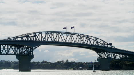 Lone-sailing-boat-beneath-Auckland-Harbour-Bridge,-New-Zealand