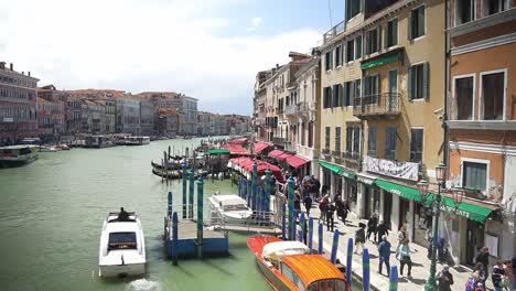 Tourists-walking-down-the-Grand-Canal-of-Venice-with-motorboat-transportation-anchored