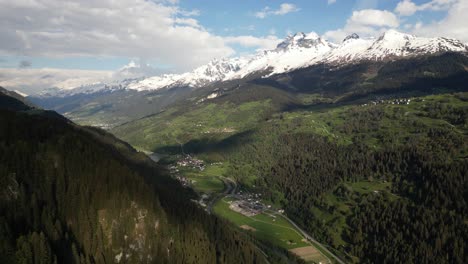 Aerial-view-of-the-valley-in-Obersaxen,-Graubünden,-Switzerland,-encircled-by-a-snow-capped-mountainous-range