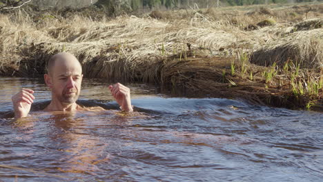 European-man-cold-plunging-in-country-stream-stands-up-and-gets-out