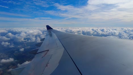 Aircraft-window-view-of-airplane-wing-and-beautiful-clouds-and-landscape-in-background