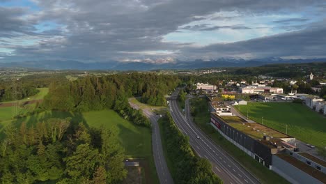 Aerial-view-of-Swiss-highway-near-green-meadow-and-forest-during-golden-hour