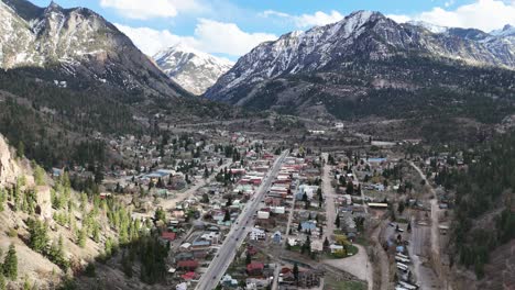 Aerial-View-of-Small-Mountain-Town,-multiple-houses-and-buildings-with-snowcapped-mountains-in-background,-Ouray-Colorado