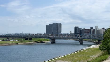 A-city-river-with-a-bridge-and-modern-buildings-under-a-partly-cloudy-sky