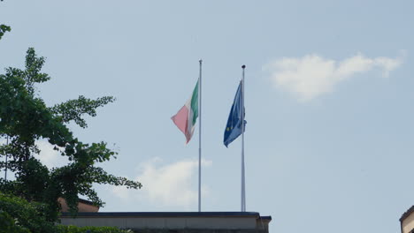 Italian-and-European-flag-waving-against-blue-sky