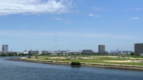Skyline-view-of-a-city-across-a-river-with-a-grassy-area-in-the-foreground-on-a-sunny-day