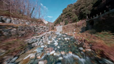 FPV-drone-view-of-a-scenic-river-flowing-through-a-rocky-forested-area-under-a-bright-blue-sky