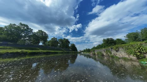 Timelapse-of-serene-waterway-with-lush-greenery-under-a-vast-sky-with-scattered-clouds