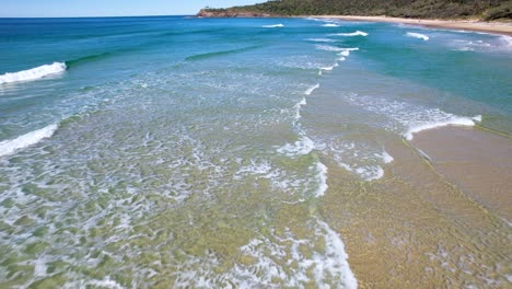 4K-Drone-video-flying-forward-over-the-blue-ocean-waves-crashing-towards-the-white-sand-beach-in-Noosa,-Queensland-Australia