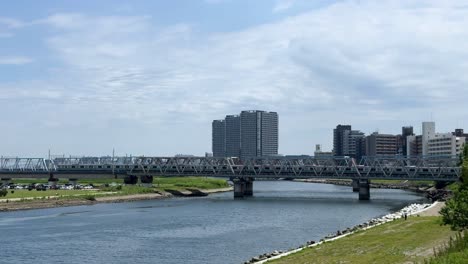 Eine-Malerische-Aussicht-Auf-Einen-Fluss-Mit-Einer-Brücke-Und-Stadtgebäuden-Unter-Einem-Klaren-Blauen-Himmel