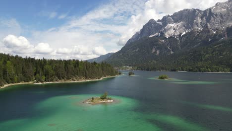 Aerial-view-of-the-colorful-Eibsee-Lake-in-Bayern,-Germany,-surrounded-by-pine-trees-and-a-distant-mountain-range,-capturing-the-essence-of-nature's-harmony-and-serenity