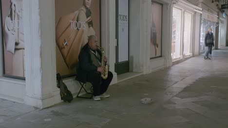 Músico-Callejero-Tocando-El-Saxofón-Fuera-De-Una-Tienda-De-Lujo-En-Venecia-Por-La-Noche