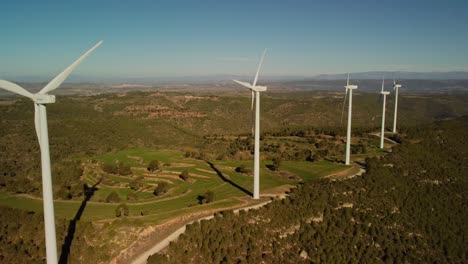 Windmills-in-Igualada,-Barcelona-on-a-sunny-day-with-green-hills-and-clear-skies,-aerial-view