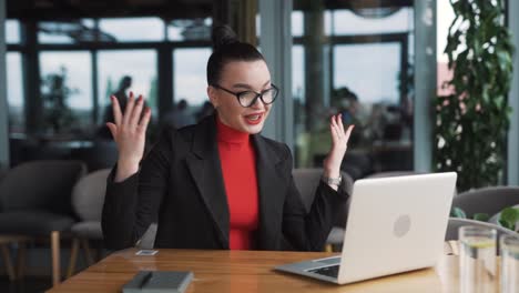 stern-young-woman-in-business-attire-argues-and-gestures-with-her-hands-during-a-video-call-on-a-laptop,-sitting-in-an-office