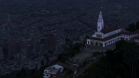 Toma-De-Drone-De-La-Iglesia-De-Monserrate-Con-Vistas-A-La-Ciudad-De-Bogotá,-Colombia-A-La-Hora-Azul.