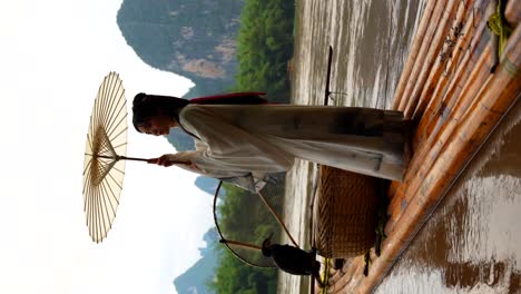 Hanfu-girl-spins-traditional-umbrella-on-bamboo-raft,-Xingping,-China