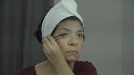Close-up-of-face-of-adult-Latina-woman-standing-in-front-of-mirror-practicing-self-makeup
