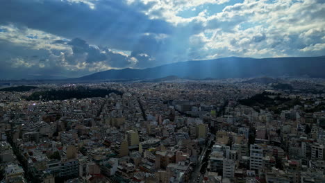 Sun-beams-shining-through-the-clouds-down-to-ancient-city-Athen,-Greece,-drone