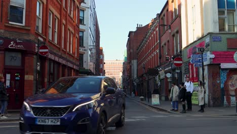 Northern-Quarter-street-scene-in-Manchester-with-people,-shops,-and-cars-on-sunny-day