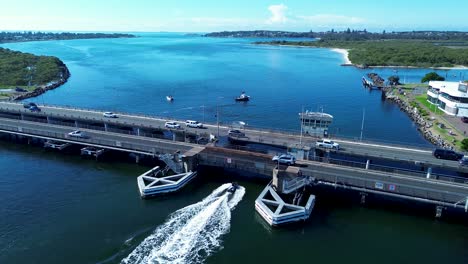 Foto-Fija-Del-Paisaje-De-Un-Barco-Que-Viaja-Bajo-La-Autopista-Puente-De-La-Carretera-En-Swansea-Canal-Entrada-Río-Belmont-Australia-Viaje-Transporte-Drone-Aéreo