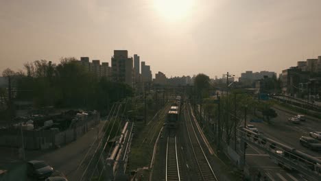 Experience-the-captivating-scene-of-a-train-swiftly-passing-by-at-dawn,-filmed-at-a-station-adjacent-to-a-highway,-where-the-early-morning