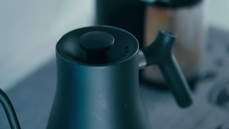 Close-up-shot-of-Black-Barista-Kettle-Lid-with-Coffee-Grinder-in-the-background
