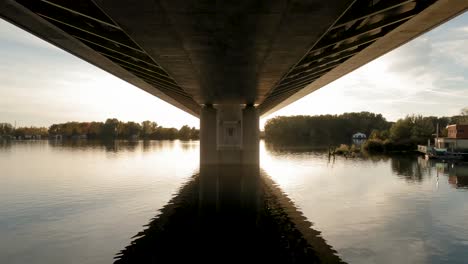 Eine-Drohne-Fängt-Einen-Ruhigen-Europäischen-Fluss-Ein-Und-Zeigt-Die-Unterseite-Einer-Brücke