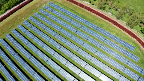 A-large-solar-farm-with-rows-of-solar-panels-on-green-grass,-aerial-view