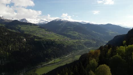 A-bird's-eye-vista-gazes-upon-Obersaxen's-valley,-ensconced-within-the-majestic-embrace-of-Graubünden's-mountain-range,-crowned-with-snow-kissed-peaks