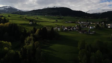 Una-Perspectiva-Aérea-Captura-Un-Pintoresco-Asentamiento-Residencial-Rodeado-Por-La-Verde-Belleza-De-Obersaxen,-Grisones,-Suiza,-Revelando-La-Tranquilidad-De-La-Vida-Alpina