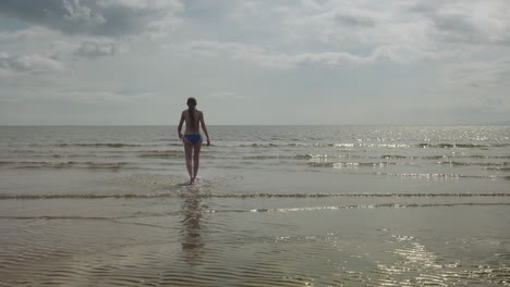 Niña-Caminando-Hacia-El-Agua-Del-Mar,-Escena-Cálida-De-Luz-Solar,-Cámara-Lenta