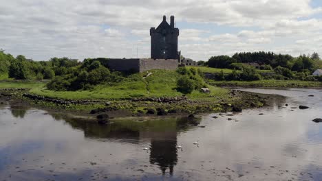 Reverse-dolly-of-Dunguaire-Castle,-Kinvara,-Galway,-with-symmetric-reflections-and-gliding-swans