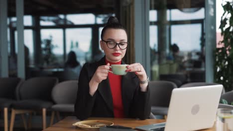 Schöne-Junge-Frau-In-Business-Kleidung-Sitzt-In-Einem-Stilvollen-Restaurant,-Arbeitet-An-Ihrem-Laptop-Und-Trinkt-Kaffee