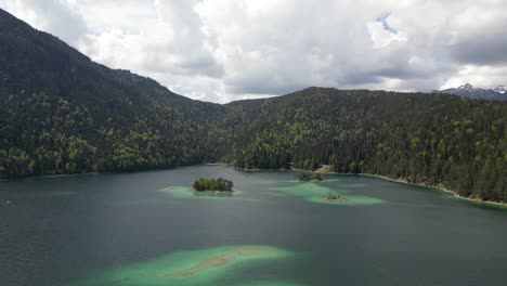 Aerial-view-of-the-vibrant-Eibsee-Lake-in-Bayern,-Germany,-surrounded-by-natural-pine-forests-and-a-distant-mountain-range,-showcasing-the-serenity-and-harmony-of-nature