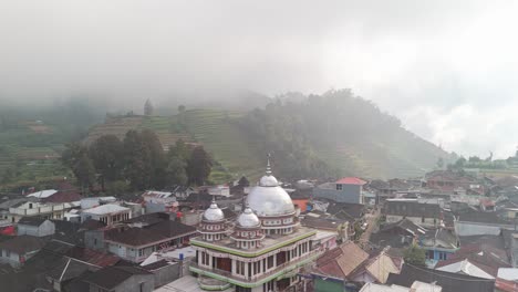 Small-town-with-central-silver-mosque-nestled-in-the-mystic-cloudscape,-volcanic-highlands-of-Dieng-Plateau,-Java,-Indonesia