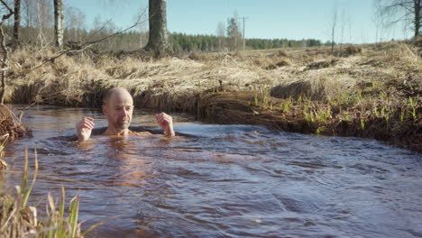 European-man-cold-plunging-in-country-stream-stands-up-and-gets-out
